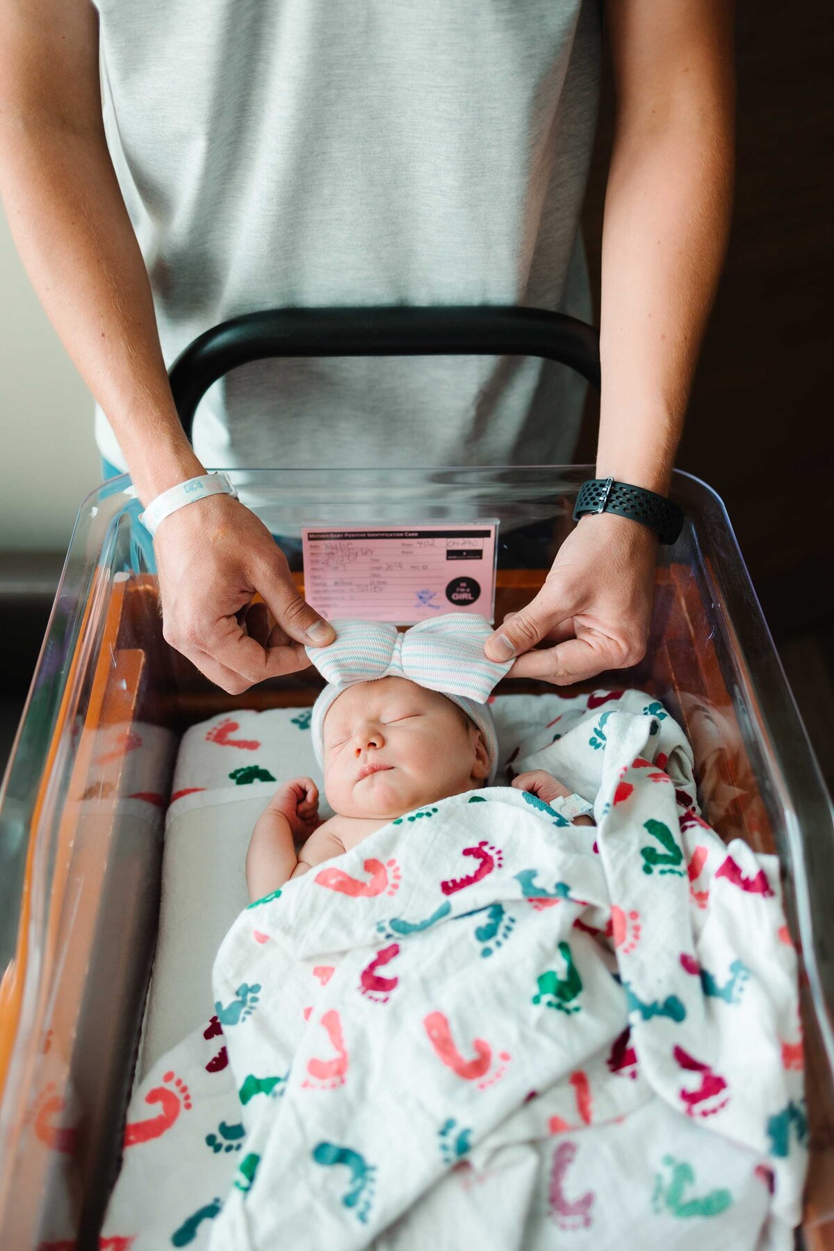 A touching moment captured by an Albuquerque photographer, featuring a newborn girl peacefully sleeping on a white blanket. Her loving dad stands behind her, providing a warm and protective presence.