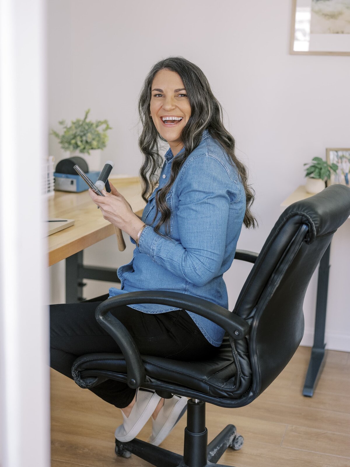 Brunette woman smiling while seated at desk with jewelry making tools during New York City brand session.