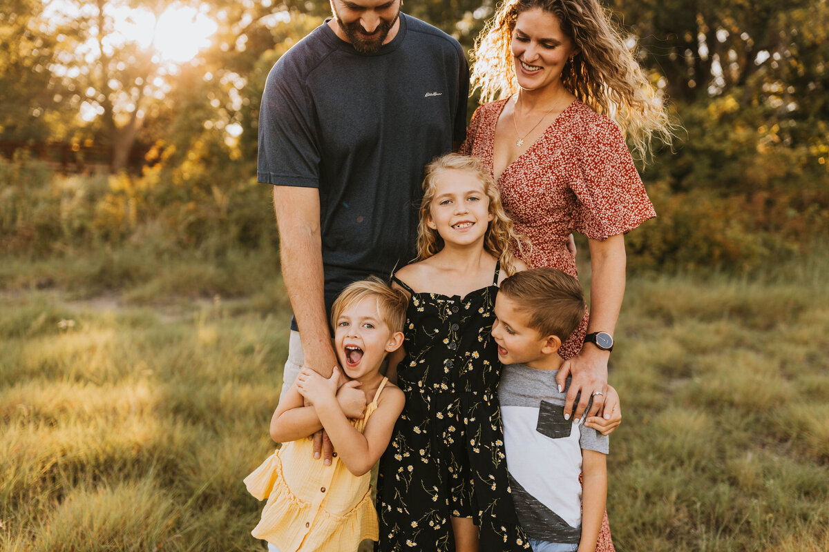 happy family standing together in a gorgeous green field at golden hour