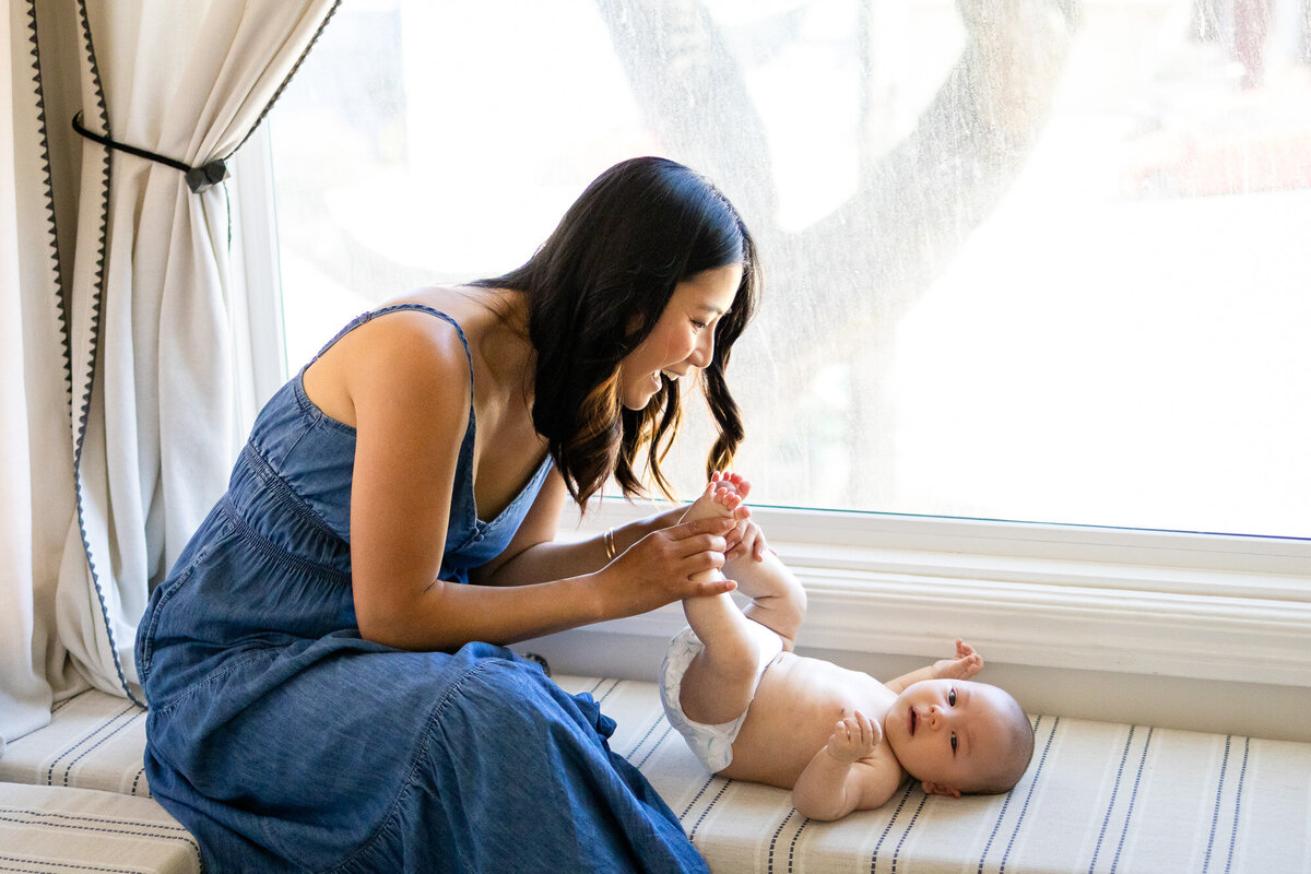 Mother beaming while holding her baby’s feet playfully, captured by San Francisco newborn photographer.