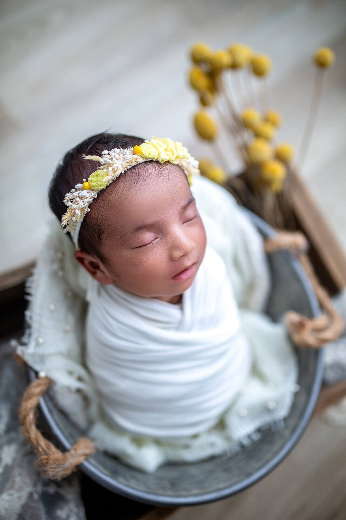 In home newborn session with little girl wrapped in white and surrounded by yellow flowers