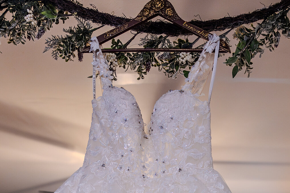 Princess wedding dress hanging on wooden hanger on branch with greenery.