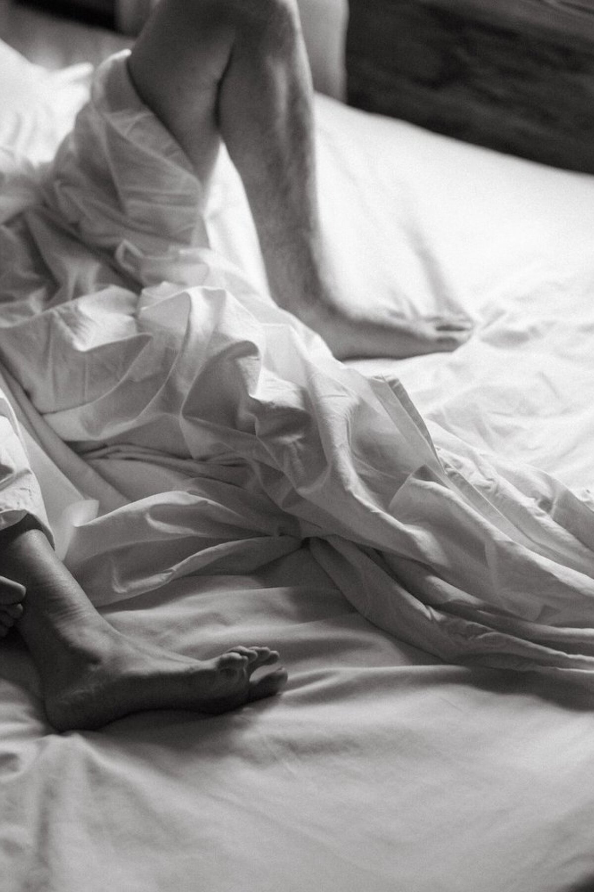 barefoot-person-resting-in-bed-with-white-sheets