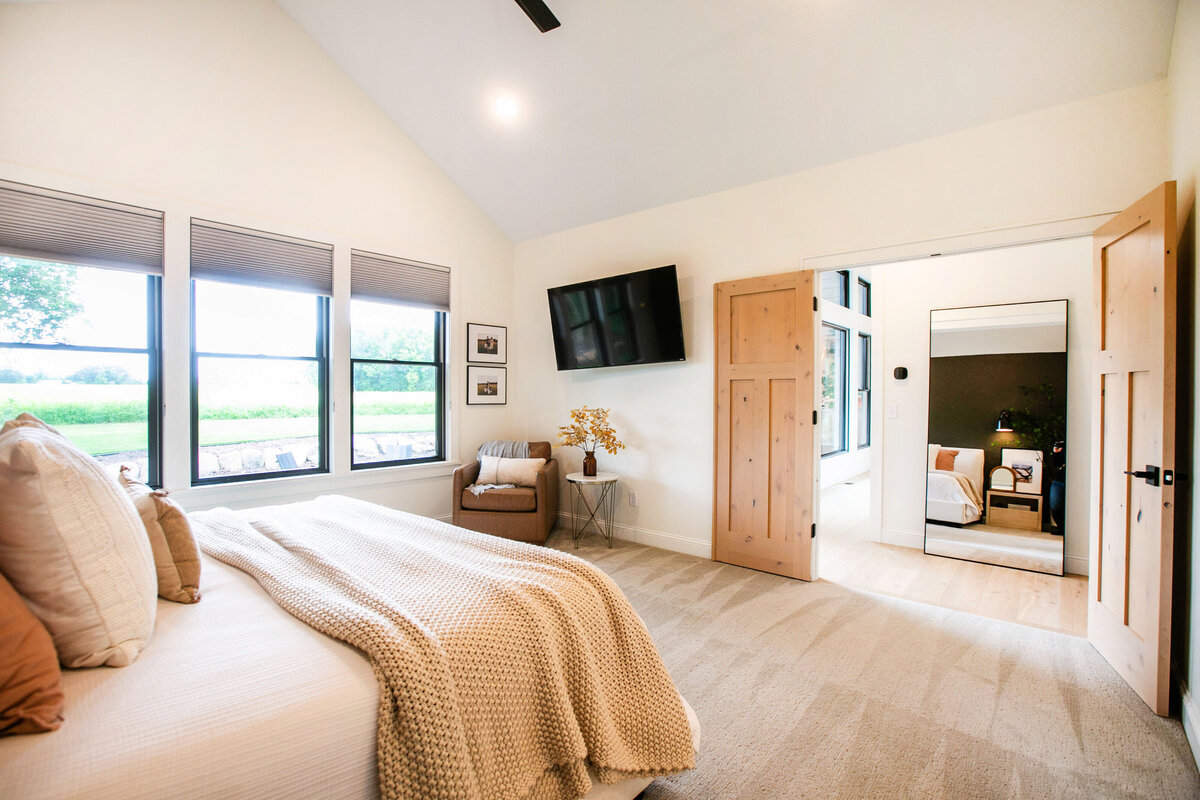 Spacious primary bedroom in custom Otsego home with natural light, wood floors and raised ceiling