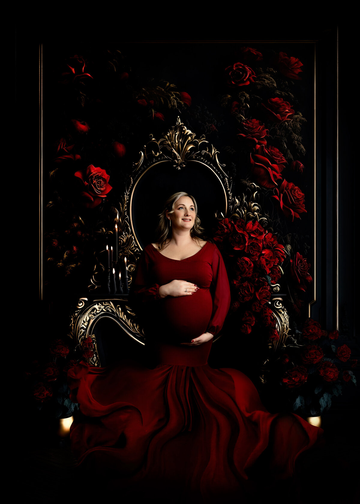A happy mother to be stands holding her bump with both hands in a red maternity gown