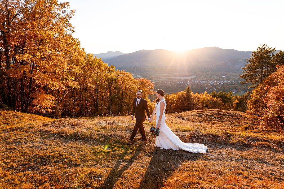 Bride and groom walking at sunset at the summit of Cranmore Mountain with beautiful fall colors by NH Wedding Photographer Lisa Smith Photography