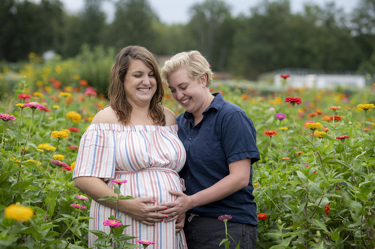 A pregnant couple smiling as they stand in a field of flowers 