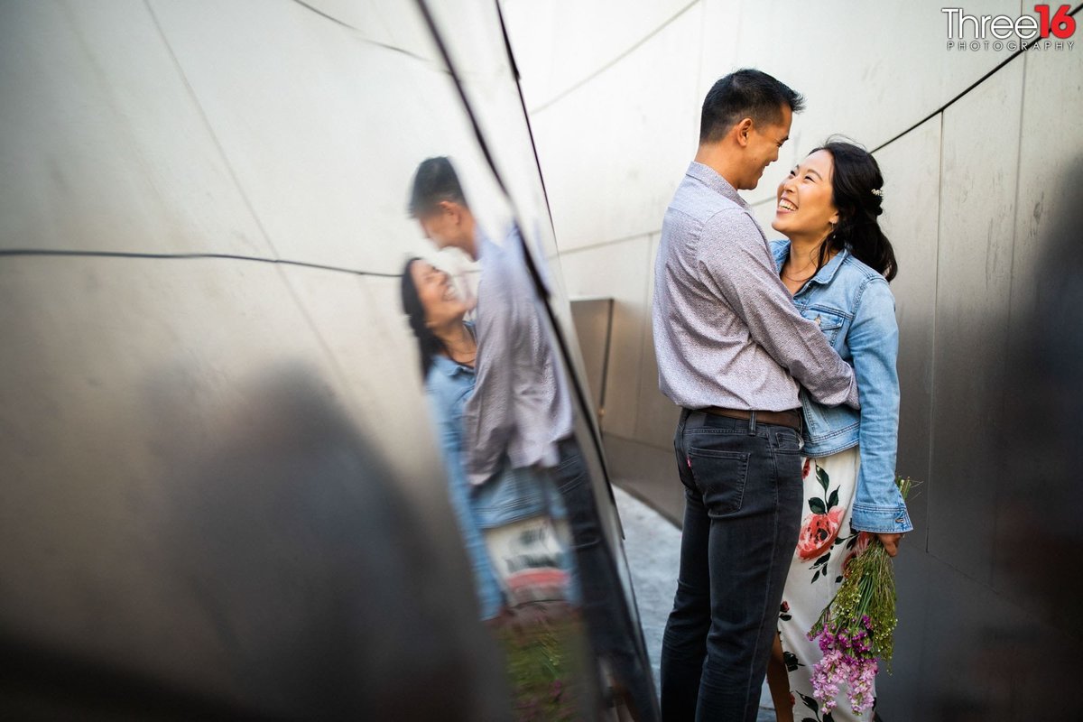 Engaged couple embrace each other between the Walt Disney Concert Hall reflection walls