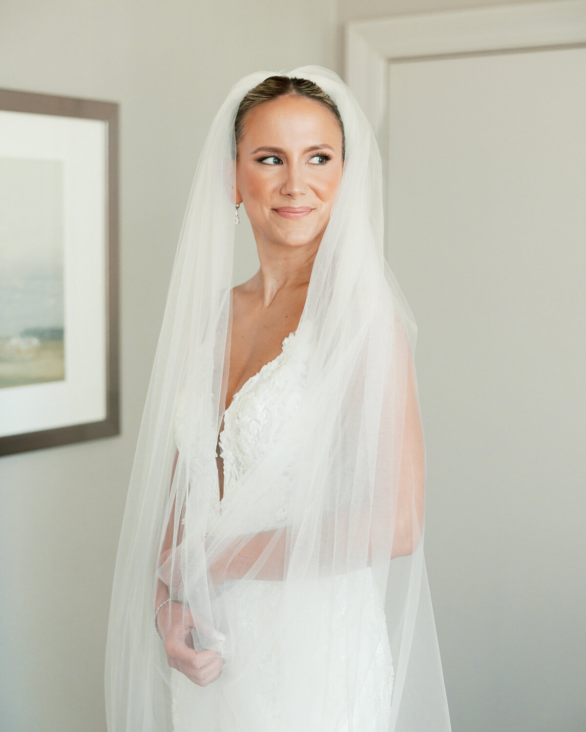 Bride in lace wedding dress and long veil smiling softly in natural light, photographed in Philadelphia.