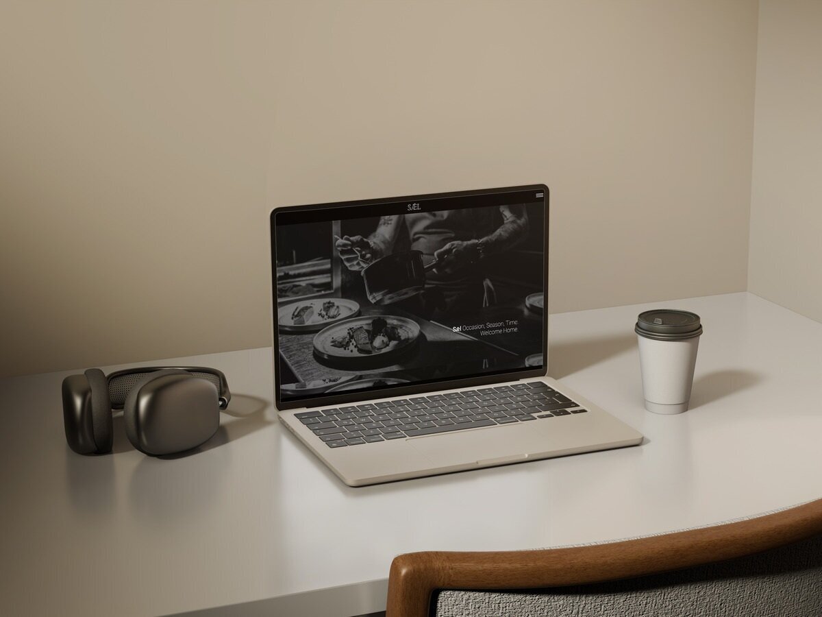 Restaurant homepage with monochrome chef image on laptop beside coffee cup and headphones.