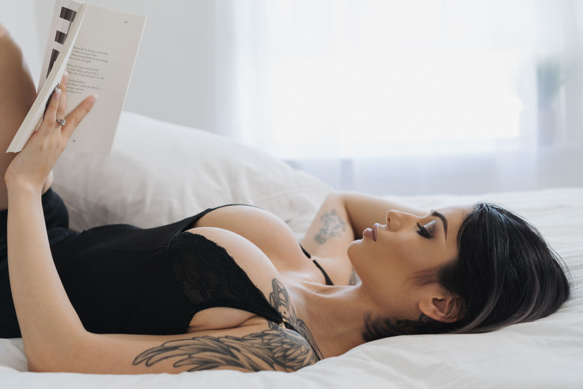 Brightly lit boudoir portrait of a woman with tattoos laying on bed