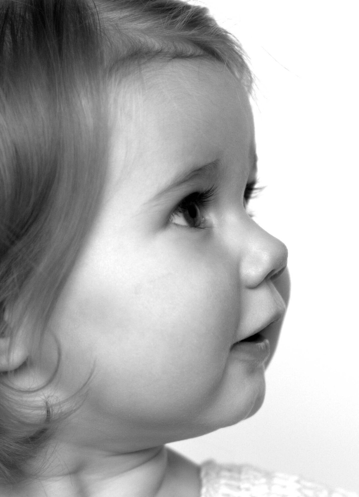 Black and white profile of a toddler with soft hair and curious expression, gazing upward against a plain background, conveying innocence.