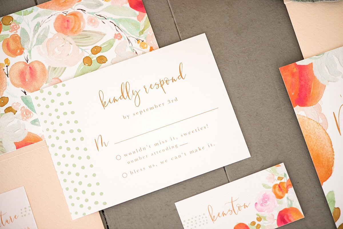 Peach themed wedding invitations decorated with peaches, blush flowers and green leaves and modern calligraphy