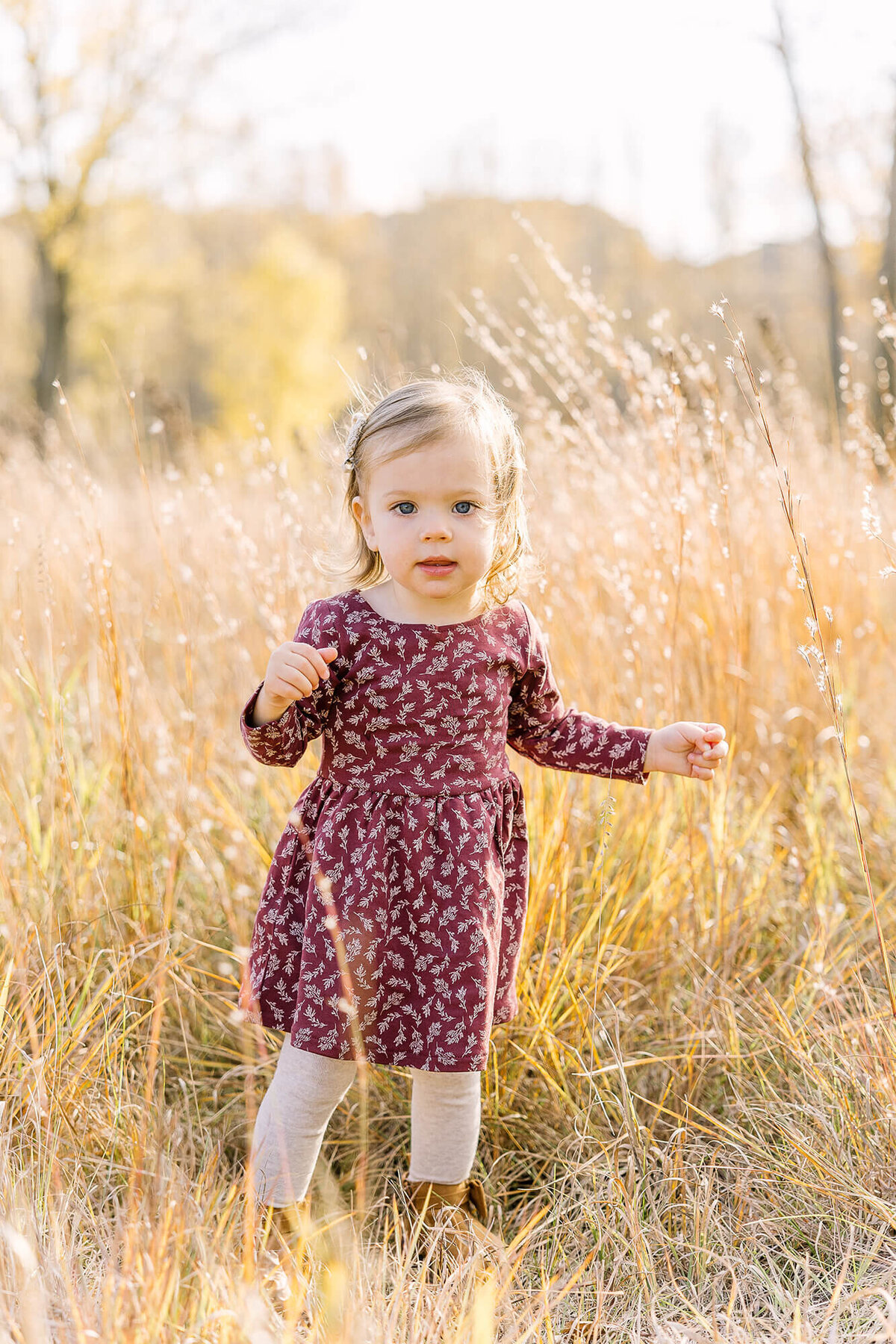 Baby girl walking through tall grass.