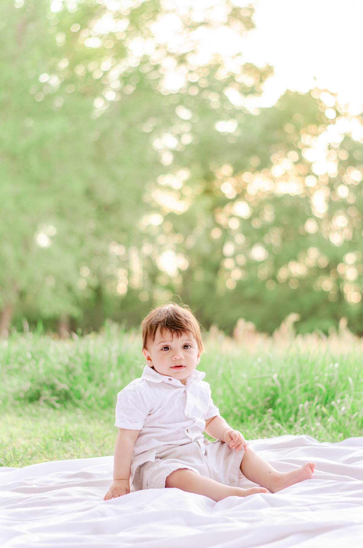 a one year old sits on a blanket with glowing bokeh behind him