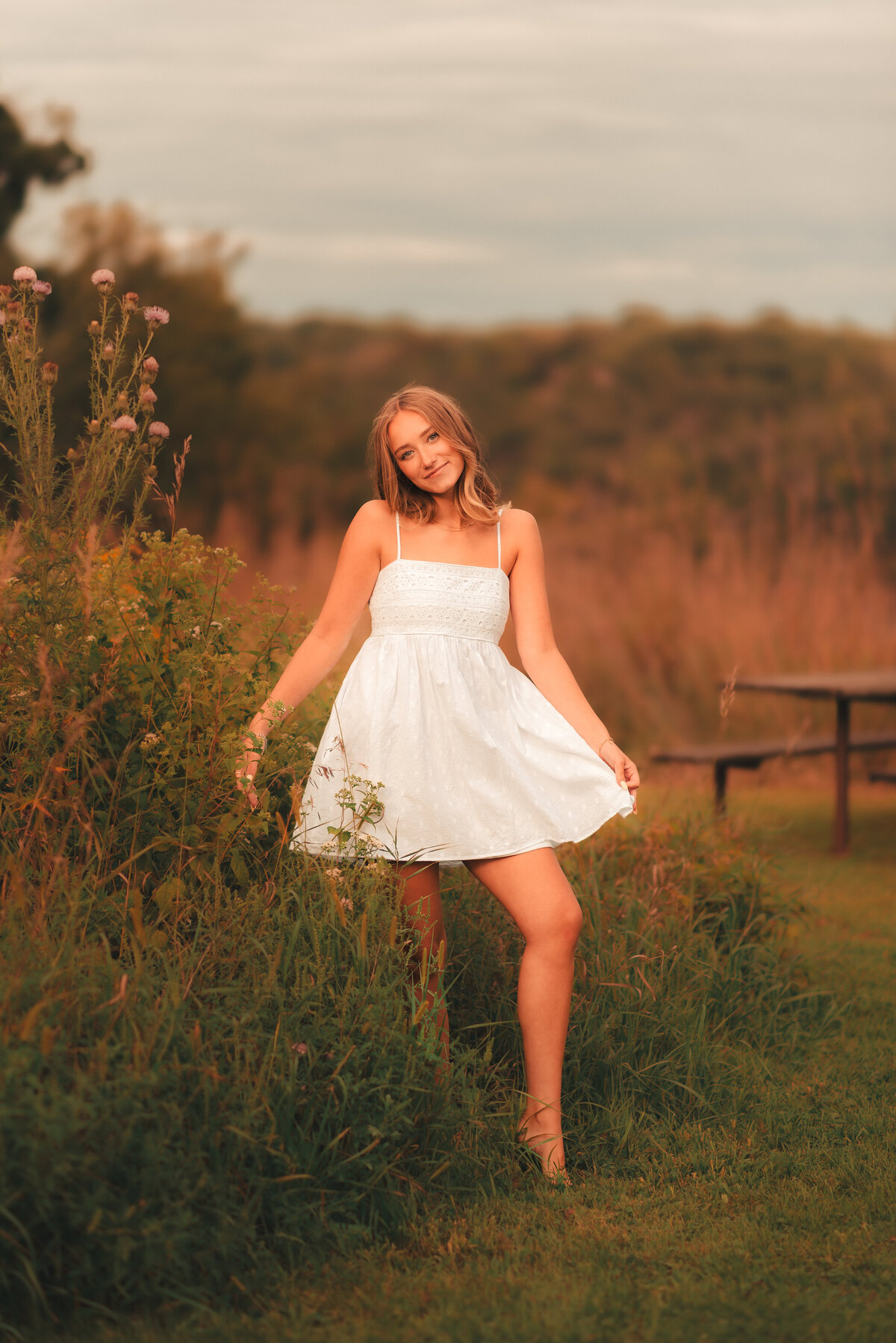 Senior photo of teen girl smiling in open meadow with summer sunlight, photographed in Minnesota.