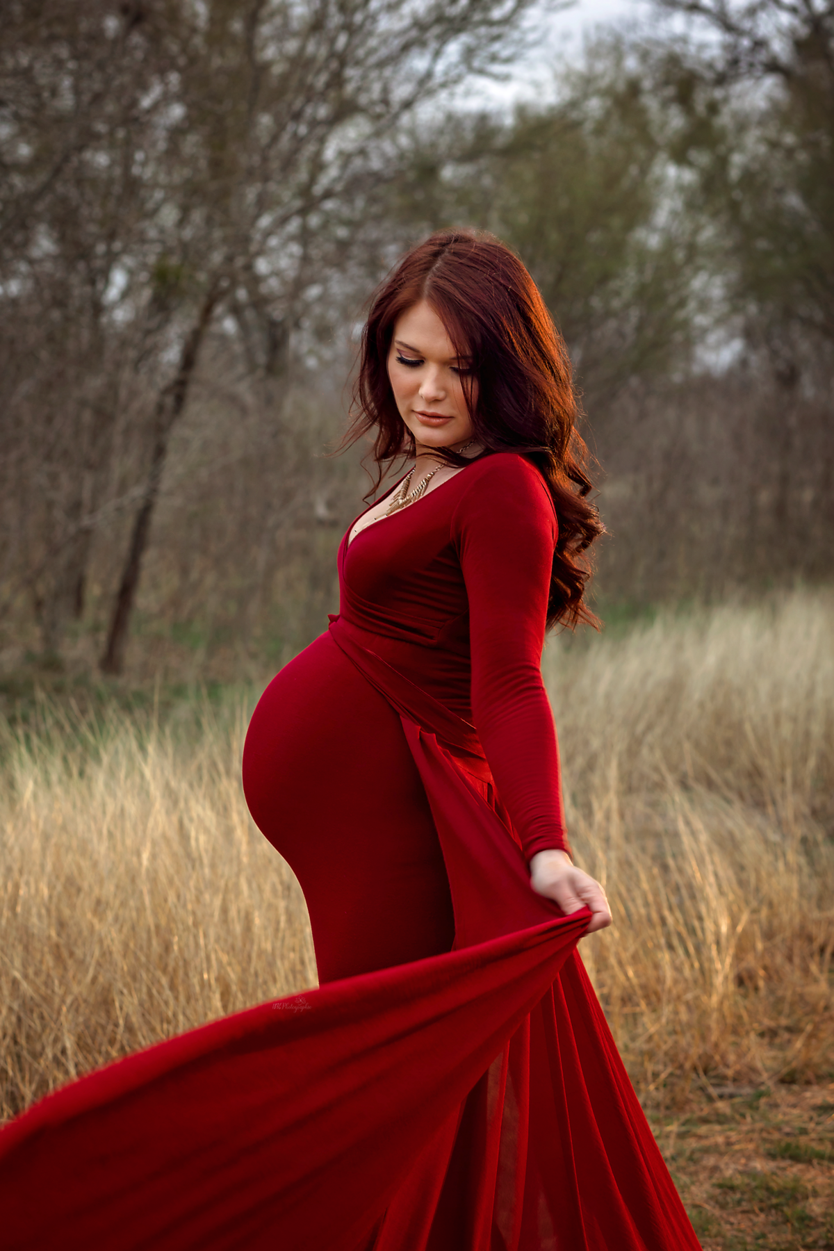 Find serenity in scarlet with our winter maternity session near San Antonio. Our mom-to-be, adorned in a flying dress, brings timeless beauty to the serene winter field backdrop.