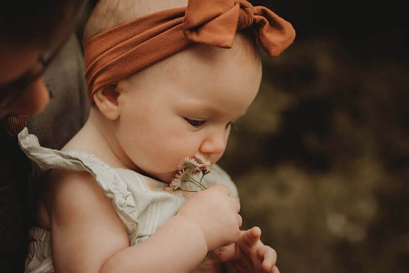 A baby girl exploring a fist full of flowers in canandaigua ny