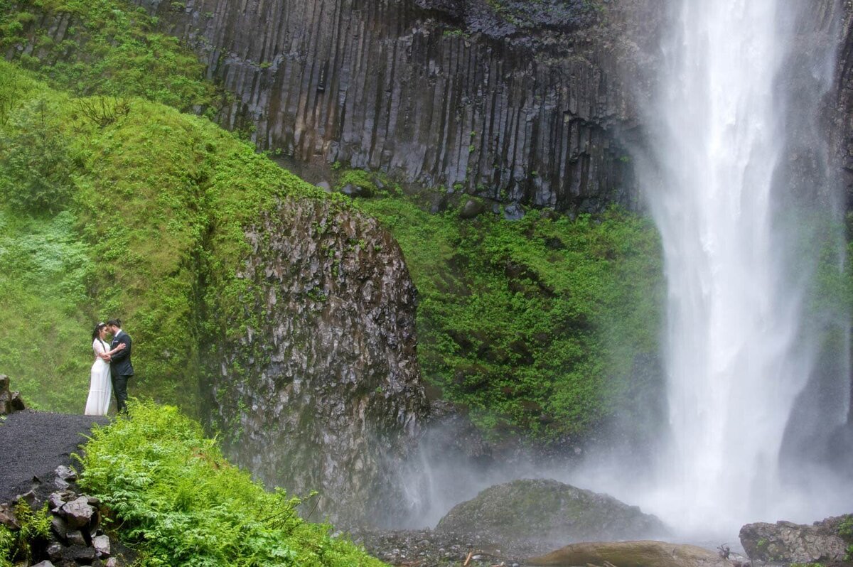 a couple stand surrounded by moss covered mountains with latourell falls coming down on one side