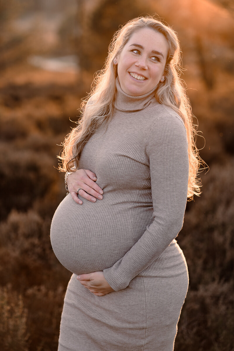 Zwangere vrouw kijkt lachend over haar schaduw terwijl ze haar handen liefdevol op haar buik heeft