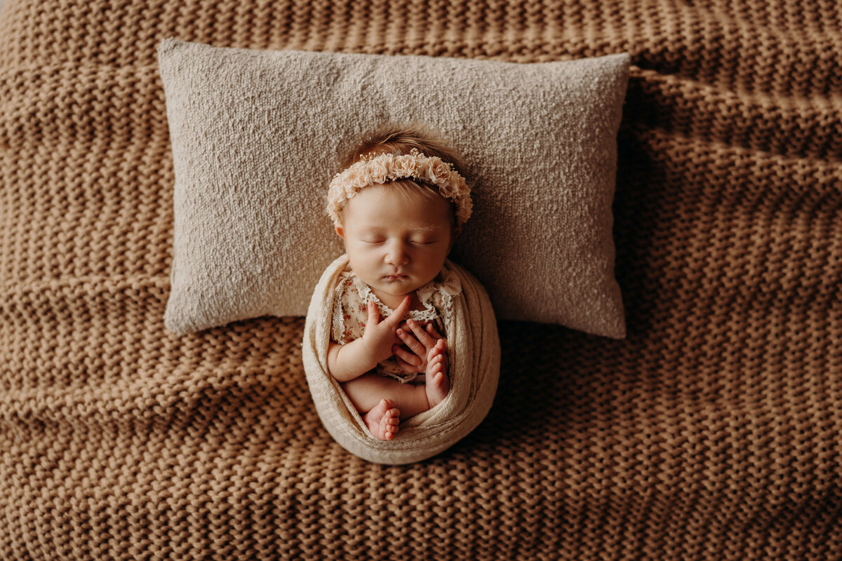 overhead view of a swaddled newborn on a tan bed