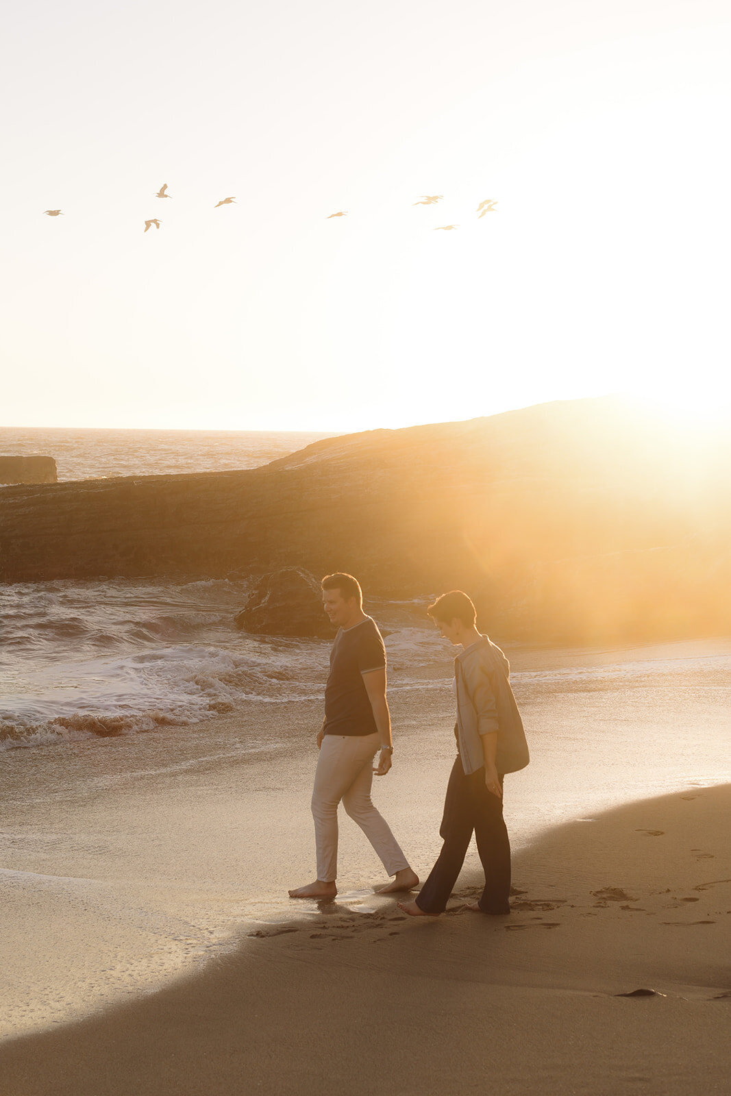 Documentary-style engagement photo of a couple walking barefoot on Panther Beach, Santa Cruz, captured during golden hour with a cinematic approach.