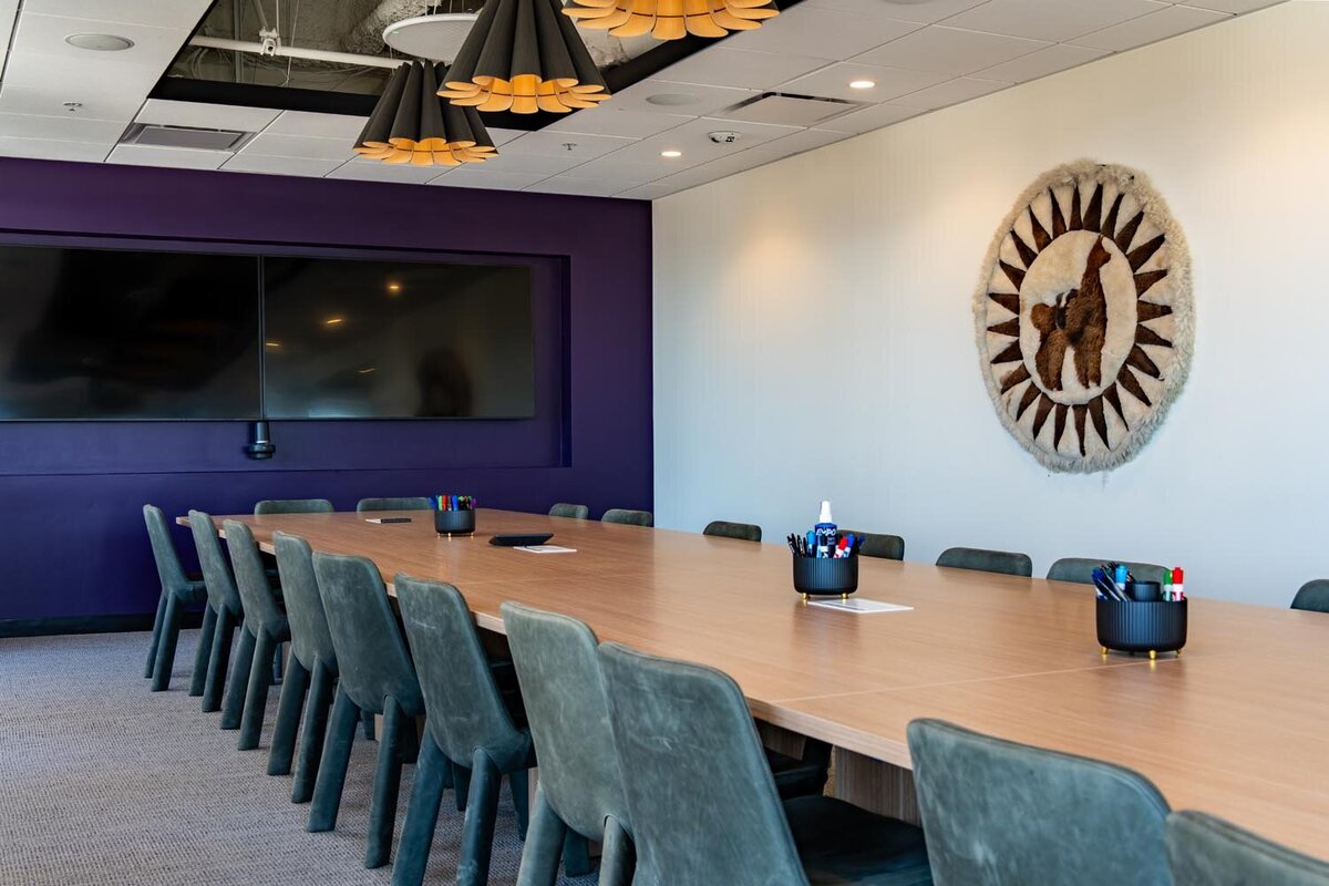 Purple-walled conference room with long wood table, modern pendant lights, and alpaca tapestry on the wall.