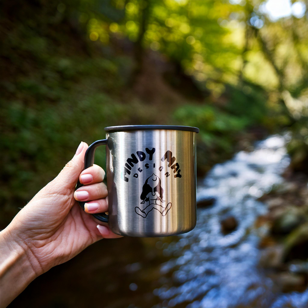 engraved-metal-camp-mug-held-up-in-front-of-a-creek