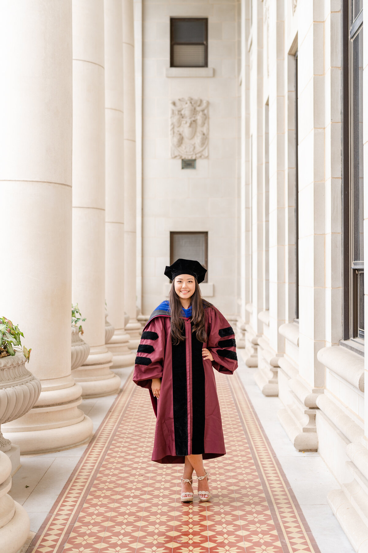 Texas A&M senior girl wearing doctorate gown, hood and cap and smiling in the columns of the Administration Building