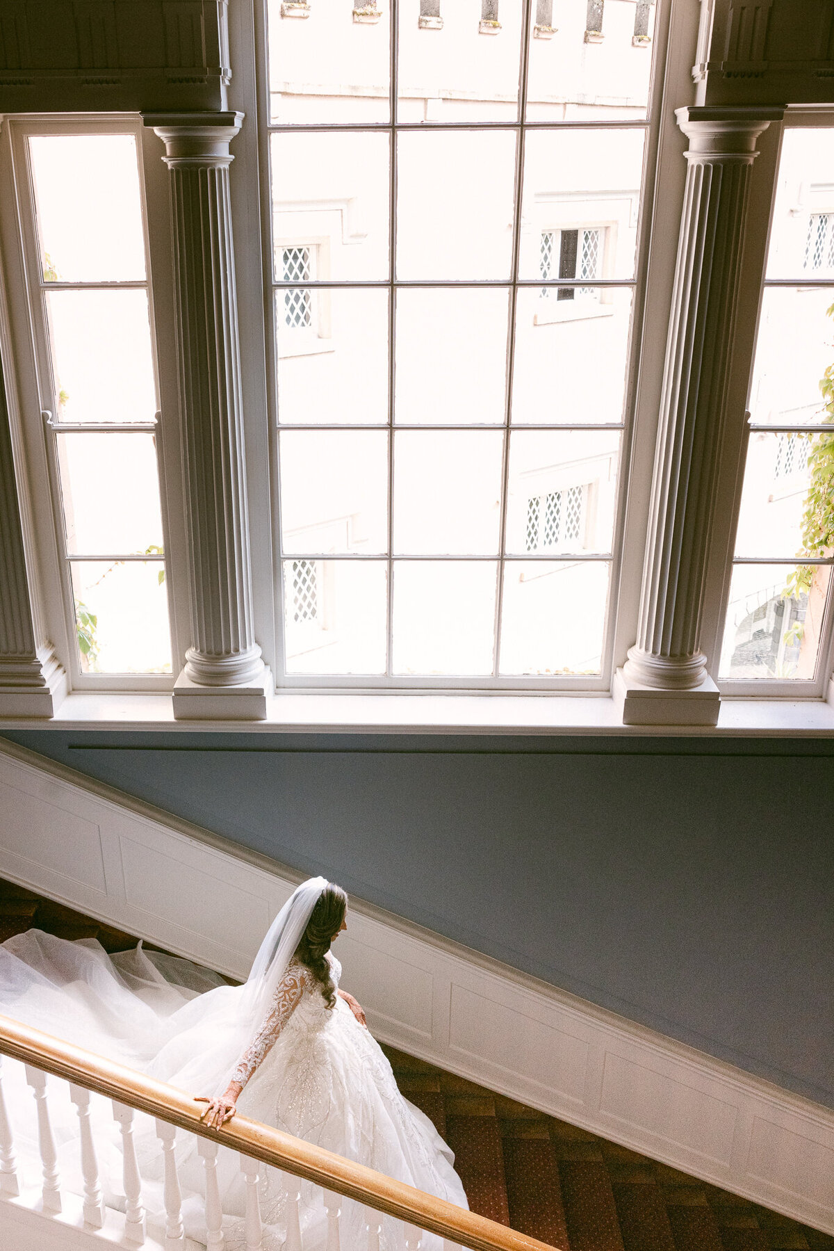 A wedding photo of the bride walking down a staircase in her white wedding dress