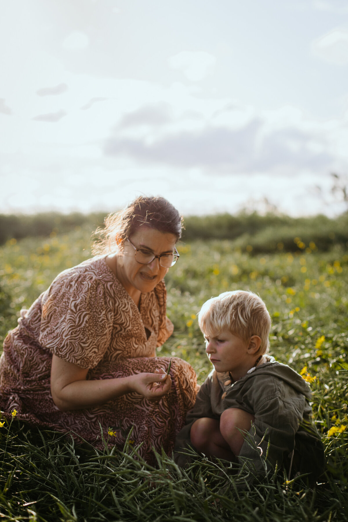 Mother and young son enjoy a nature moment as she presents a flower to him in the grass.
