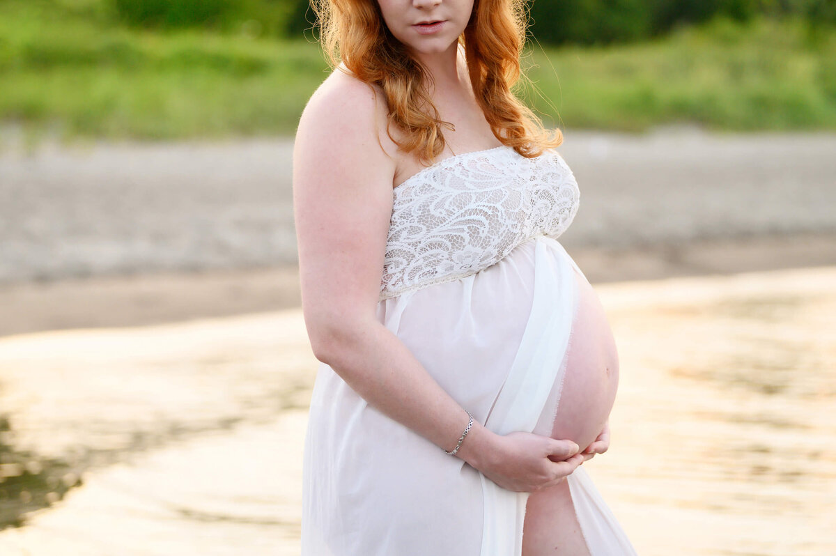 Beach maternity photograph session with red-haired mom wearing a white maternity dress.