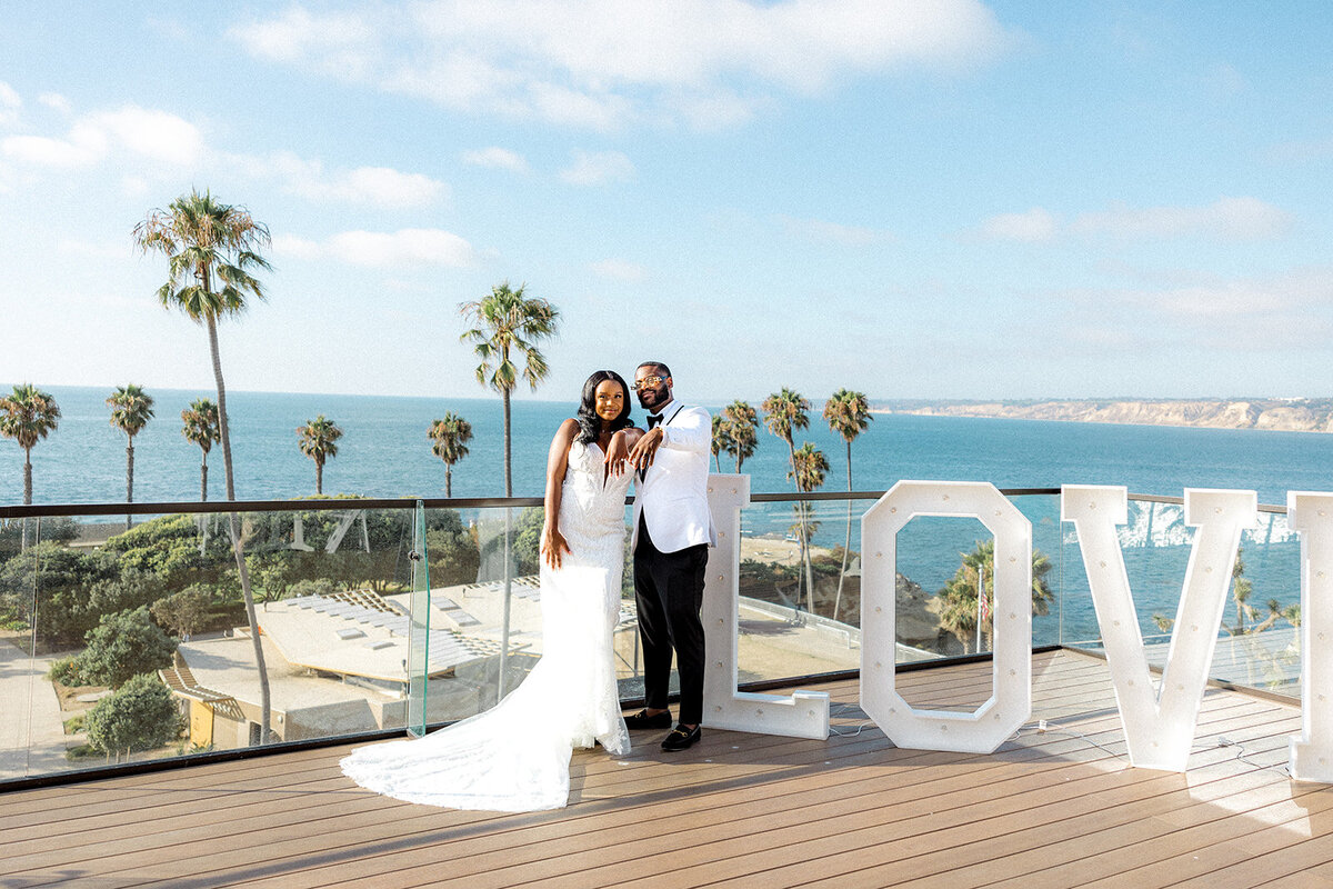 Bride and groom next to "LOVE" sign with ocean in the back in San Diego
