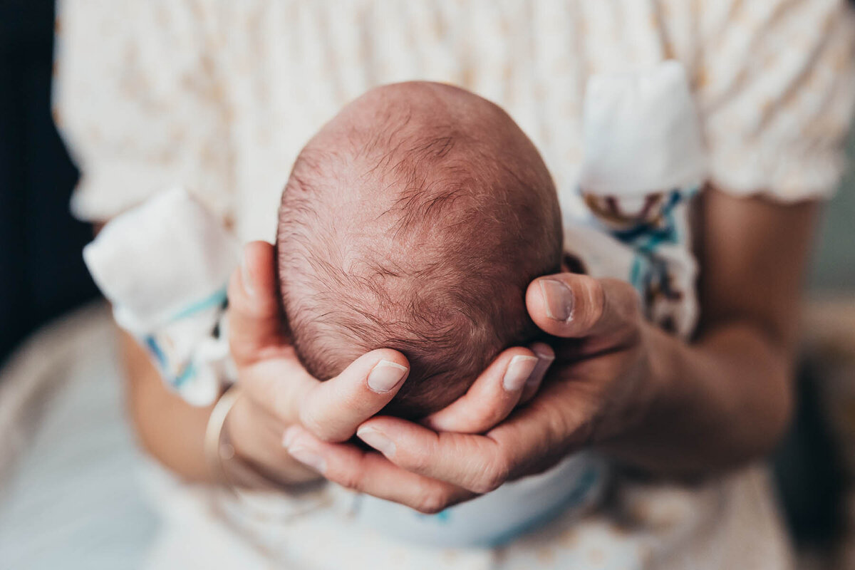 a close up of a newborn baby head held in his mother's hands.