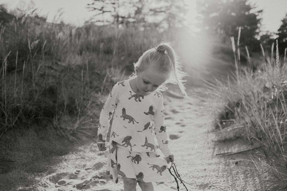 4-year girl standing and looking down with a stick in her hand and sun shining behind her in Yyteri in Finland