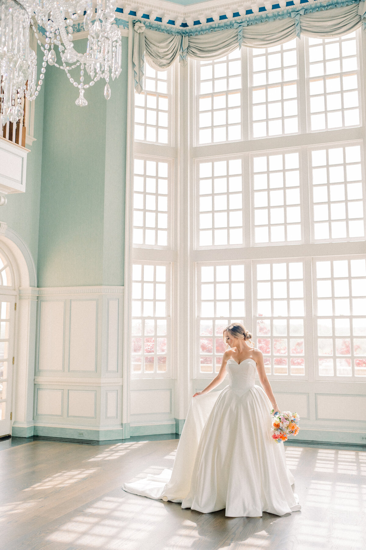 Bride swishing her dress in an elegant ballroom with floor to ceiling windows at the estate at river run