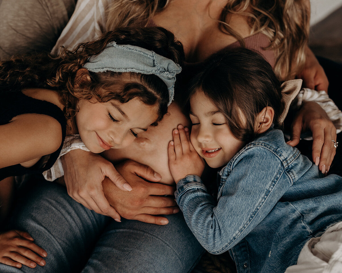 two big sisters hug their mom's expectant belly