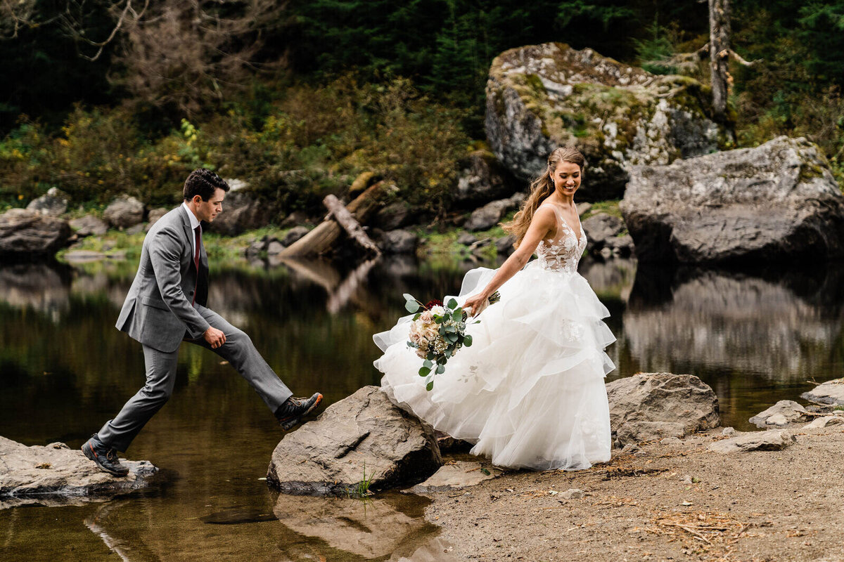 A bride and groom walk over rocks on a crystal clear backcountry lake in the Washington cascades photographed by pacific northwest elopement photographer amy galbraith