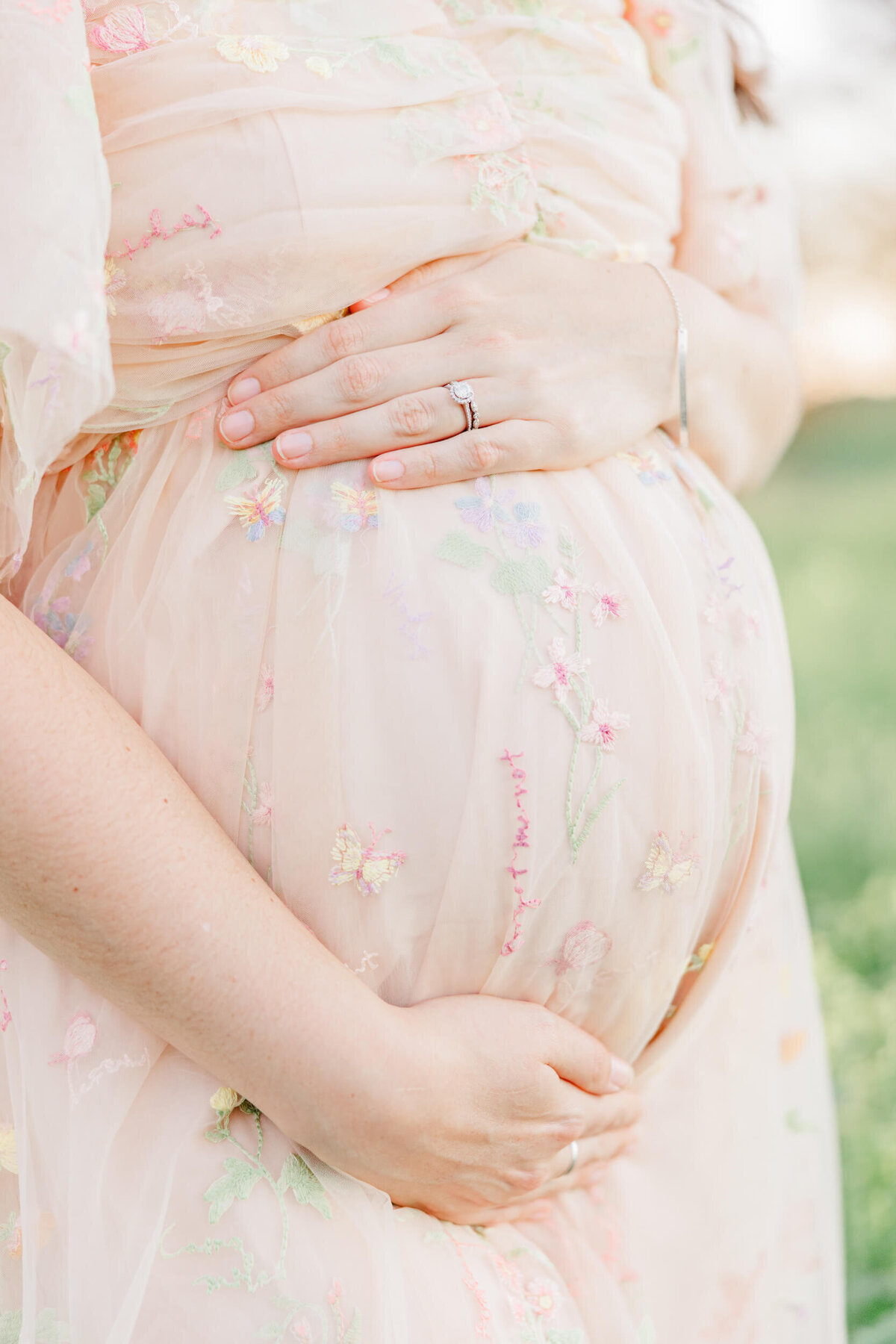 Closeup of the baby bump of a mama in a soft pink dress with a delicate embroidered floral pattern