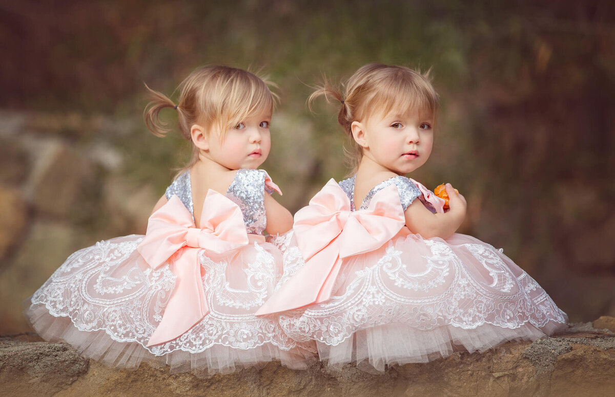 Twins Taytum and Oakley sitting on a wall and looking over their shoulder at the camera - Los Angeles Children’s Photographer