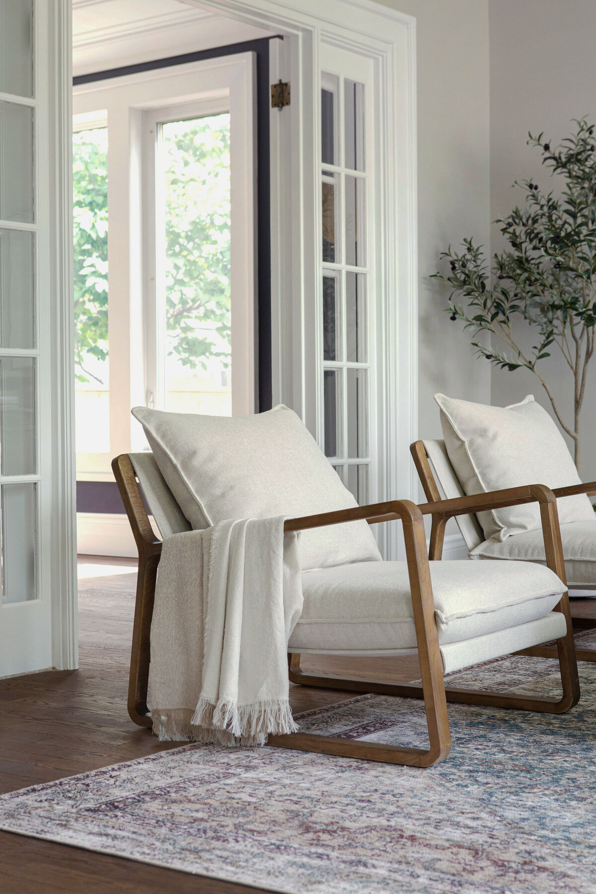 living room staged with walnut and beige upholstered armchairs in front of french doors