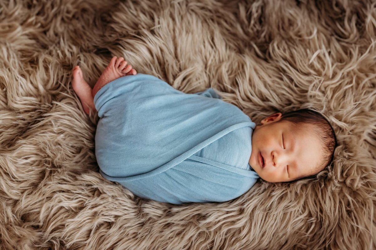 baby boy in blue swaddle sleeping on tan fur rug