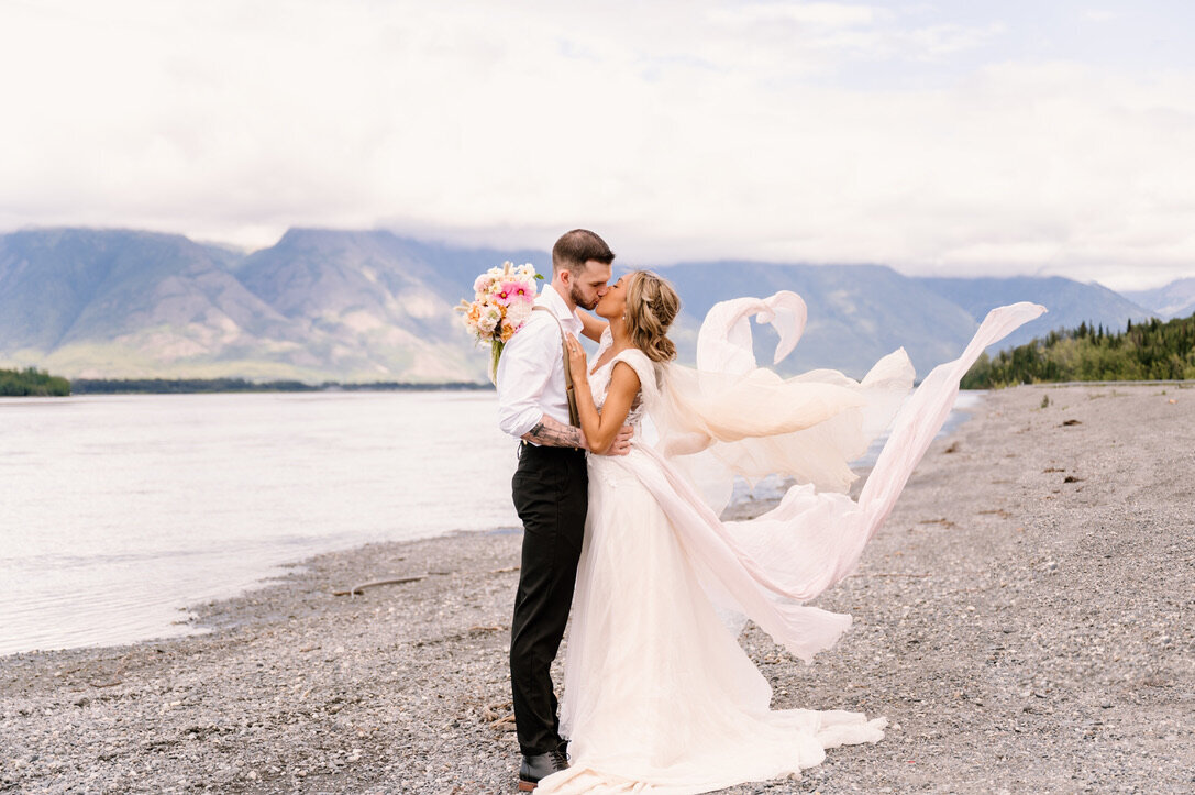 bride and groom kissing near lake in Alaska