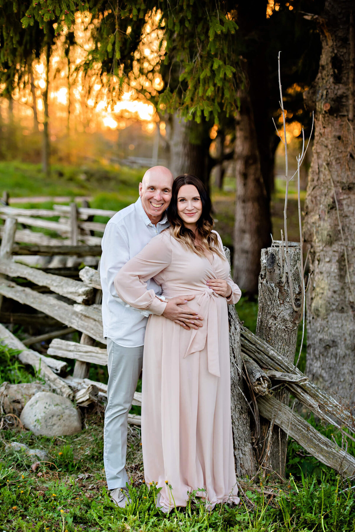 husband standing behind his pregnant wife holding her belly for their Toronto summer maternity photos.