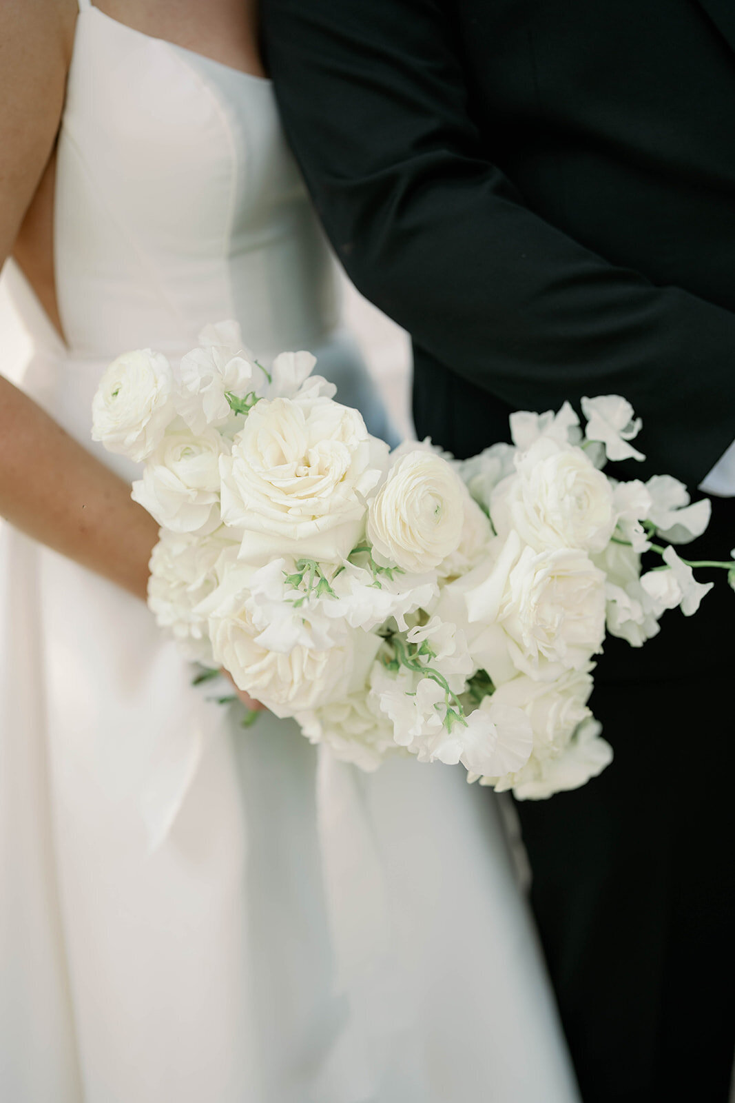 Close-up photo of bride holding classic white rose bouquet, elegant bridal details.
