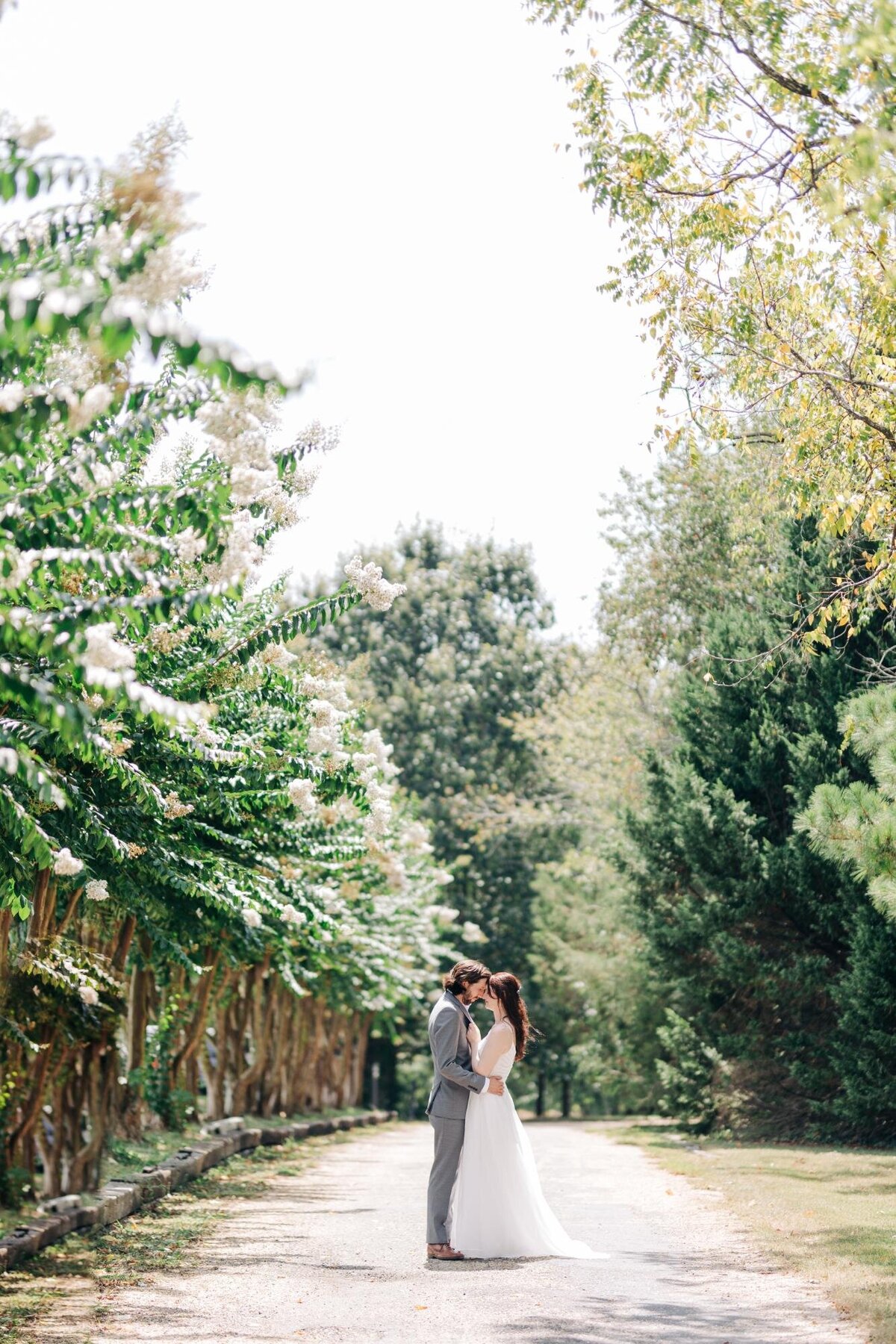 A couple in wedding attire embracing on a tree-lined path.