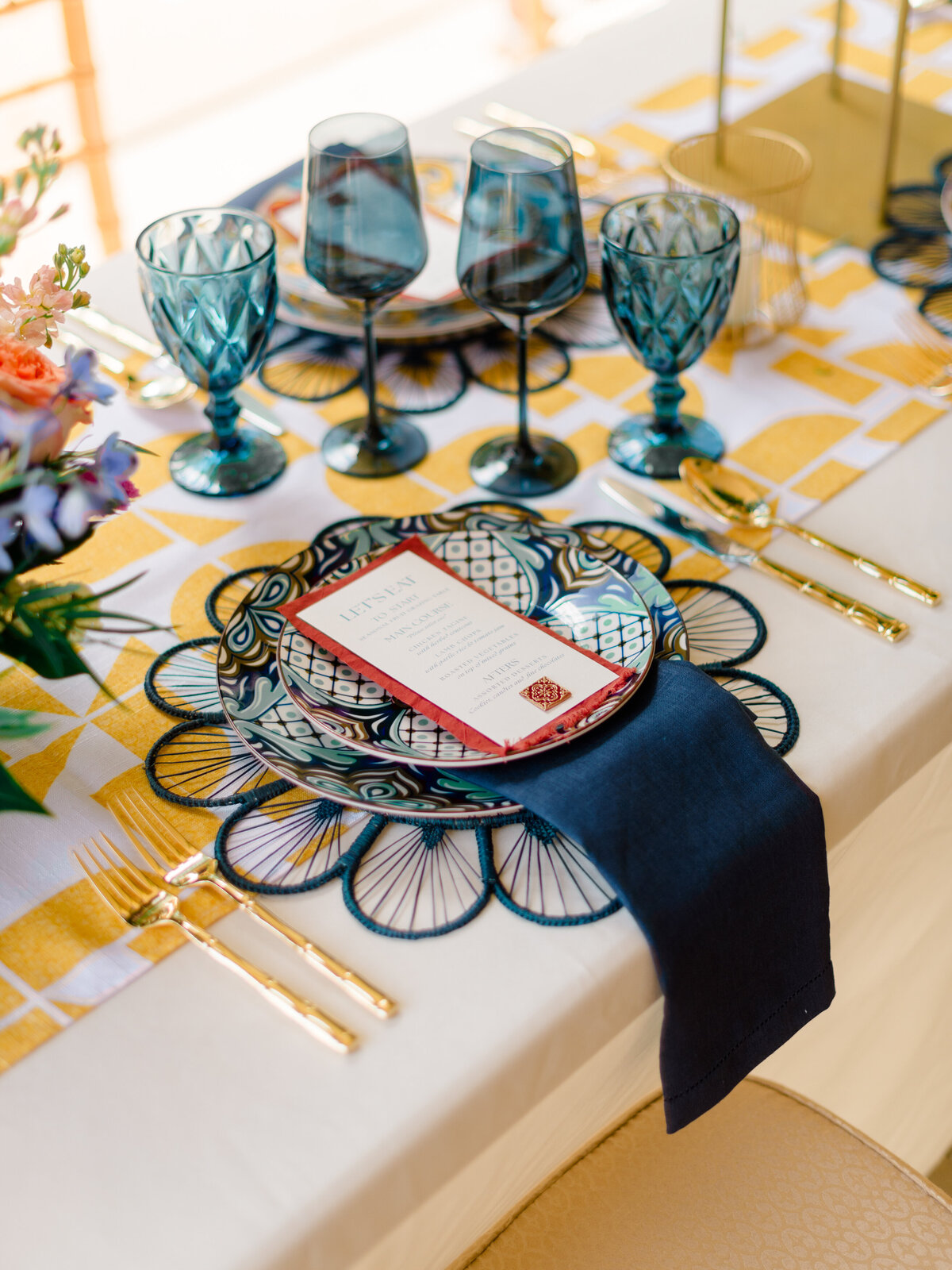 Close-up of a vibrant and eclectic wedding tablescape at Cairnwood Estate, featuring patterned ceramic plates, navy linen napkins, gold flatware, and textured teal glassware. Captured by Elizabeth Kane Photography, a Philadelphia Fine Art Wedding Photographer, this editorial showcases bold yet refined table styling for elegant East Coast weddings.