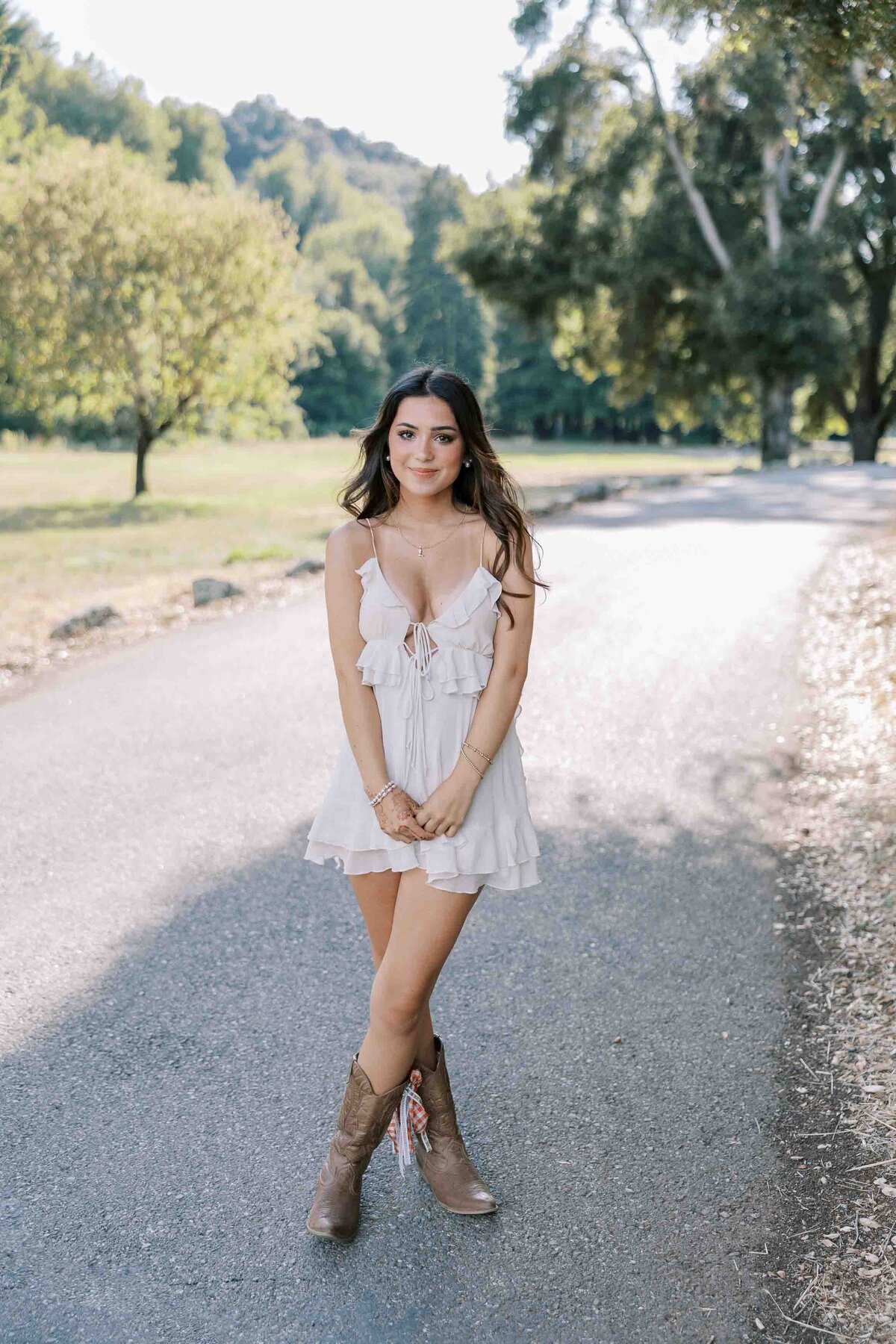 Brunette girl wearing a white dress and cowboy boots and holding her hands in front of her