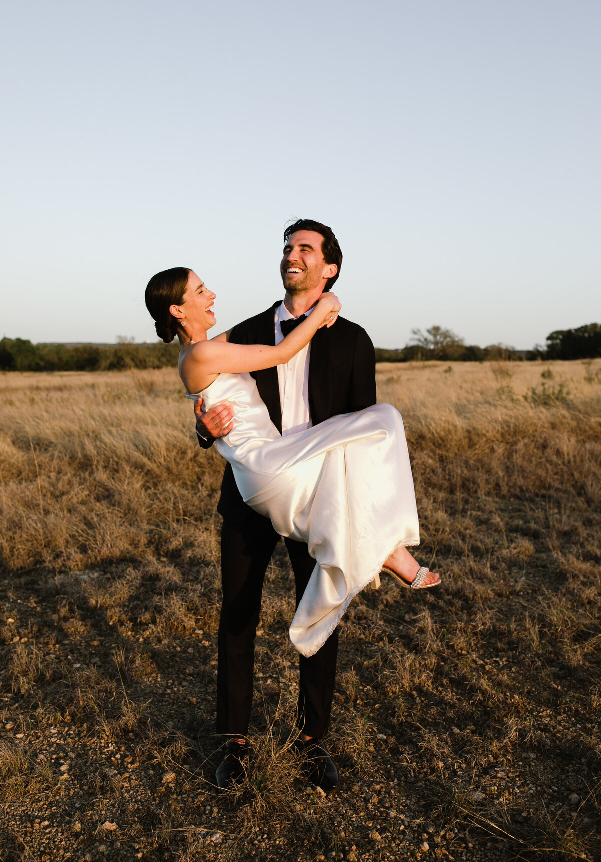 Groom carrying bride in his arms through a field