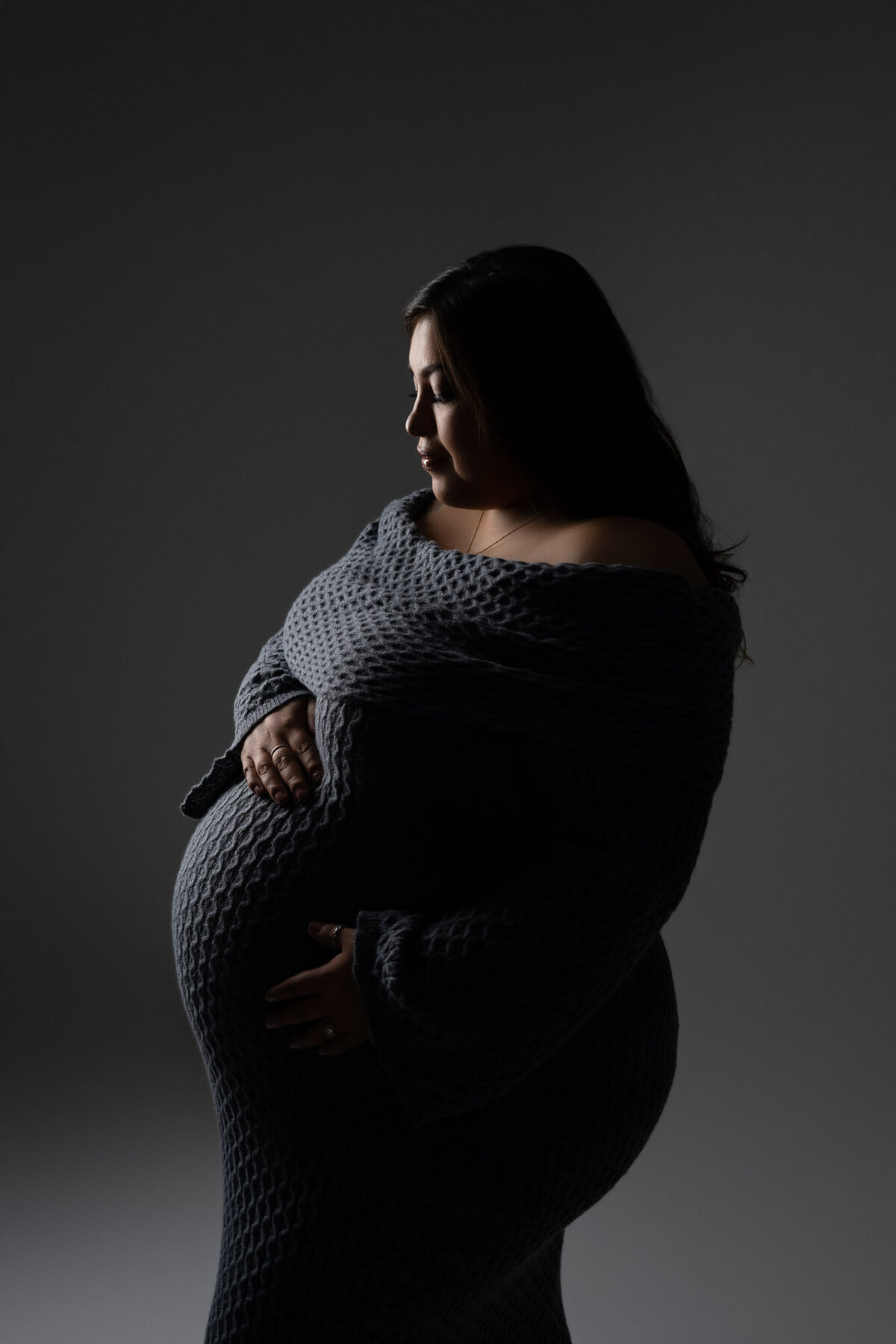 Professional maternity portrait of expectant mother in dark attire with studio lighting